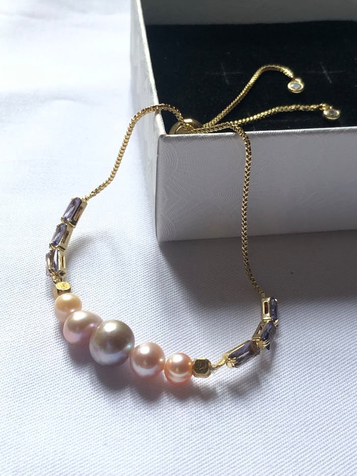 Close-up of a pearl and gemstone bracelet elegantly designed with a gold chain on a white background.