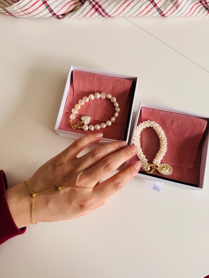 Hand model displaying pearl bracelets with gold accents in open gift boxes.